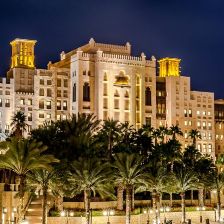 A stunning night view of a luxurious hotel with palm trees reflecting on water in Dubai.